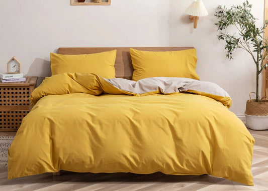 Yellow bedding set on a bed in a bedroom with a side table and plant.